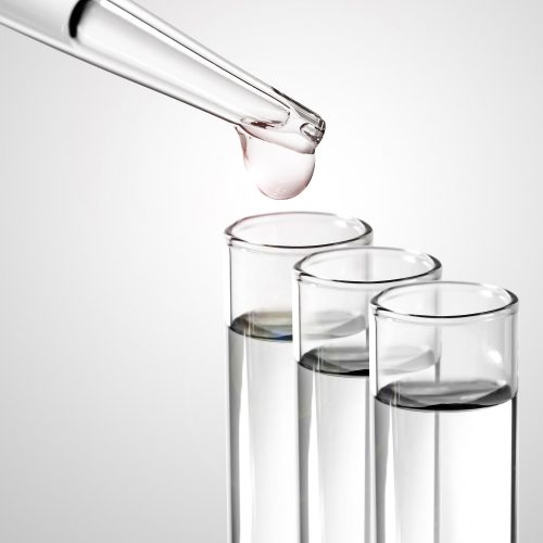 Laboratory pipette with drop of chemical liquid  over glass test tubes